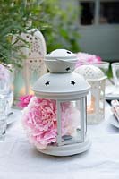 Table decorated with an eclectic mix of white lanterns and peonies, with peonies inside one of the lanterns
