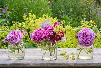 Summer floral arrangement in glass jars with roses, alchemilla mollis, Dianthus barbartus, sweet peas and fragaria barbartus