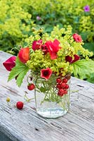 Summer floral arrangement in glass jar with red sweetpeas, potentilla, fragaria vesca, red currants and alchemilla mollis