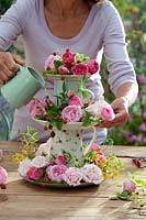 Woman arranging flowers on tiered stand made from jugs and plates