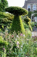 Hanham Court Gardens, Bristol. Early summer garden with topiary 'chess pieces' and mixed informal planting at base