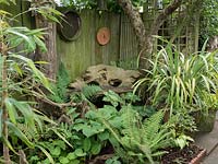 Hidden in the shade is a rustic wooden bench.  The fence is also decorated with rustic garden implements