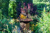 Bird bath of Corten steel on oak plinth in the Front Garden. Veddw House Garden, Monmouthshire, South Wales. 