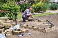 Woman hammering metal stakes into bottom of raised bed to secure into the ground
