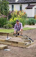 Woman adding the second layer of wooden blocks onto the raised bed