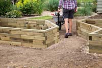Woman walking away from home constructed wooden raised bed with her tools
