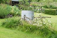 Old galvanised water bowser surrounded by long grass and Ox eye daisies.