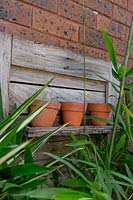 A recycled timber shelf display mounted to a brick wall with three decorative terracotta pots.