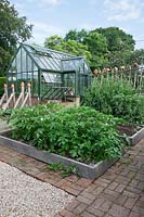 Greenhouse in kitchen garden, brick paved with oak sleeper raised beds, planted with Potatoes and Sweet Peas on hazel support.