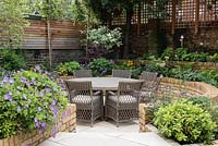 Late Summer garden with seating area and raised beds with Geranium 'Rozanne' and Choisya 'Aztec Pearl'