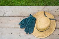 Summer hat and suede gardening gloves on wooden surface