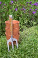Teracotta pots and a rustic hand fork on grass