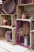 Vintage wooden crate storage with various pots, garden welly boots, a rustic watering can and Allium seed heads