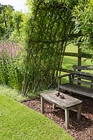 A seating area nestled in the shade of a woven Willow arch
