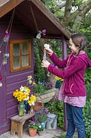 Young girl decorating her playhouse with small vases on string and flowers