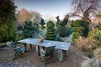 Table and chairs and Yew and Box topiary in Charlotte and Donald Molesworth's garden, Kent, UK.