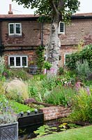 A small low maintenance modern cottage garden planted with self seeding annuals and  perennials. A two tier pond water feature of brick and lead. Lead container filled with Lavender, Stipa tenuissima, Lychnis coronaria, Verbena hastata, Verbena bonariensis.