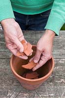 Man adding crocks to empty pot prior to planting to aid drainage