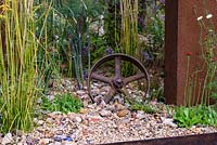 Rusted metal wheel in gravel garden - Brownfield Metamorphosis. RHS Hampton Court Palace Flower Show 2017 - Designer: Martyn Wilson. Sponsor: St. Modwen Properties PLC