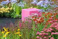 Decorative pink cubed seating and colourful borders with Helenium 'Moerheim Beauty', Penstemon 'Garnet', Agapanthus 'Blue Triumphator', Verbena bonariensis and Imperata cylindrica 'Rubra' - Colour Box garden - RHS Hampton Court Palace Flower Show 2017 - Designers: Charlie Bloom and Simon Webster.