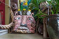 Carved and painted wooden tiger head outside the front door, with skull vases perched on top. Ginger plant - Hedychium sp. in the foreground. Sculptor and ceramicist Marcia Donahue's garden in Berkeley, California.