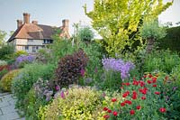 The Long Border in May with Papaver commutatum 'Ladybird', Cotinus, Spirea japonica, Geranium, Honesty, Gladiolus, Alliums. Great Dixter, Sussex