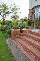 The brick steps from the crochet lawn to the patio are decorated with ceramic pots both freestanding and hung from the wall