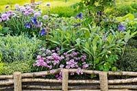 Woven screen fencing a raised bed of mixed herbs and spring flowers including pink Dianthus. Bridgend College: The Life of a Hermit. Designer: Matthew Joseph, RHS Cardiff Show 2017