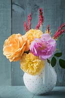 Bouquet of yellow, orange, pink scented roses  and Persicaria amplexicaulis - red bistort in white porcelain vase against dark wooden background.