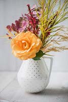 Bouquet of autumn flowers including orange scented rose, Persicaria amplexicaulis - red bistort, Hydrangea paniculata, Amsonia hubrichtii and dried flowers of Stipa gigantea in a vase against white wooden background.
