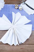 Making a paper pom pom from napkins. The 2 fastened strips of folded napkins should fold up in to a fan shape