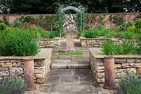 The herb garden in walled kitchen garden with focal point Armillary Sphere by David Harber. Raised beds made of drystone walls, with herbs including Chives, Mint and Monarda surrounded by Lavandula 'Imperial Gem'. Steel arches with Sweet Peas and decorative chimmney pots.