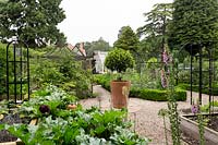 General view across vegetable garden towards glass house, with gravel paths and raised beds and box lined beds