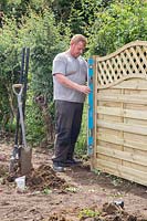 Man using spirit level to ensure post and fencing panel is straight