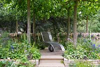 The Poetry Lover's Garden - Steel chaise longue under Lime trees, Tilia x europaea -  RHS Chelsea Flower Show 2017