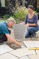 Woman and Man working together laying patio by adding mortar 