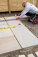Man using rubber mallet and spirit level to ensure new paving is level 