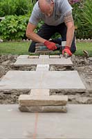 Man using rubber mallet and spirit level to ensure new paving is level 