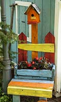 A colourful wooden chair with a container planted with Begonia