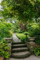 Narrow garden with a stone path, mixed shrub borders and small lawn