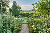 Double borders with roses, foxgloves, Crambe cordifolia, delphiniums and astrantias with a view of the open countryside landscape
