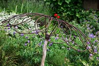 Rusted umbrella shaped metal and wood  sculpture in flower border.