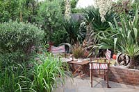 Striped director chairs and small table with Yucca gloriosa flowering in late summer. Bronze Phormium, grasses and small variegated Yucca. Fishing net and rope decorations. 
