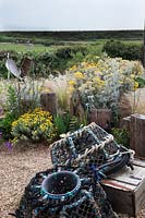 Seaside themed front garden planted with coastal plants  including Cineraria 'Silver Dust', Santolina 'Lambrook Silver' , Stipa tenuissima, Verbena bonariensis and decorated with   driftwood sculptures and lobster pots with a sea view.