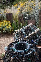 Lobster pots in seaside themed front garden planted with coastal plants  including Cineraria 'Silver Dust', Santolina 'Lambrook Silver' , Stipa tenuissima, Verbena bonariensis and decorated with   driftwood sculptures