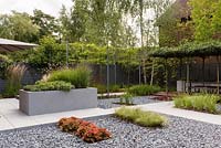Modern garden with porcelain paving and black washed riverstone pebbles. Plants include: Calamagrostis x acutiflora 'karl foerster', Carex comans 'amazon mist', Heuchera 'marmalade', Kniphofia 'flamenco', Molinia caerulea, Pennisetum thunbergii 'red buttons', Photinia x fraseri 'red robin', Salvia officinalis 'kew gold' and Thymus 'silver queen'