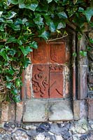 Terracotta plaques with shields of arms, in 'Medieval ' terrace wall, framed by Hedera helix - ivy. 