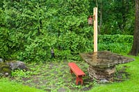 Flagstone patio with red wooden sitting bench and stone slab table bordered by Thuja occidentalis - Cedar hedge in residential backyard in late spring, Quebec, Canada.