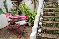 Seating area with metal pink garden table and chairs by steps in urban garden, July