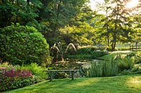 Pond area with herbaceous borders, woods, bench and water feature. Dina Deferme garden, June